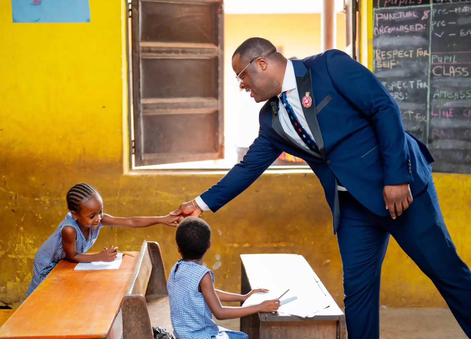 Dr Paddy Iyamu reaching out to shake the hand of a pupil at her desk