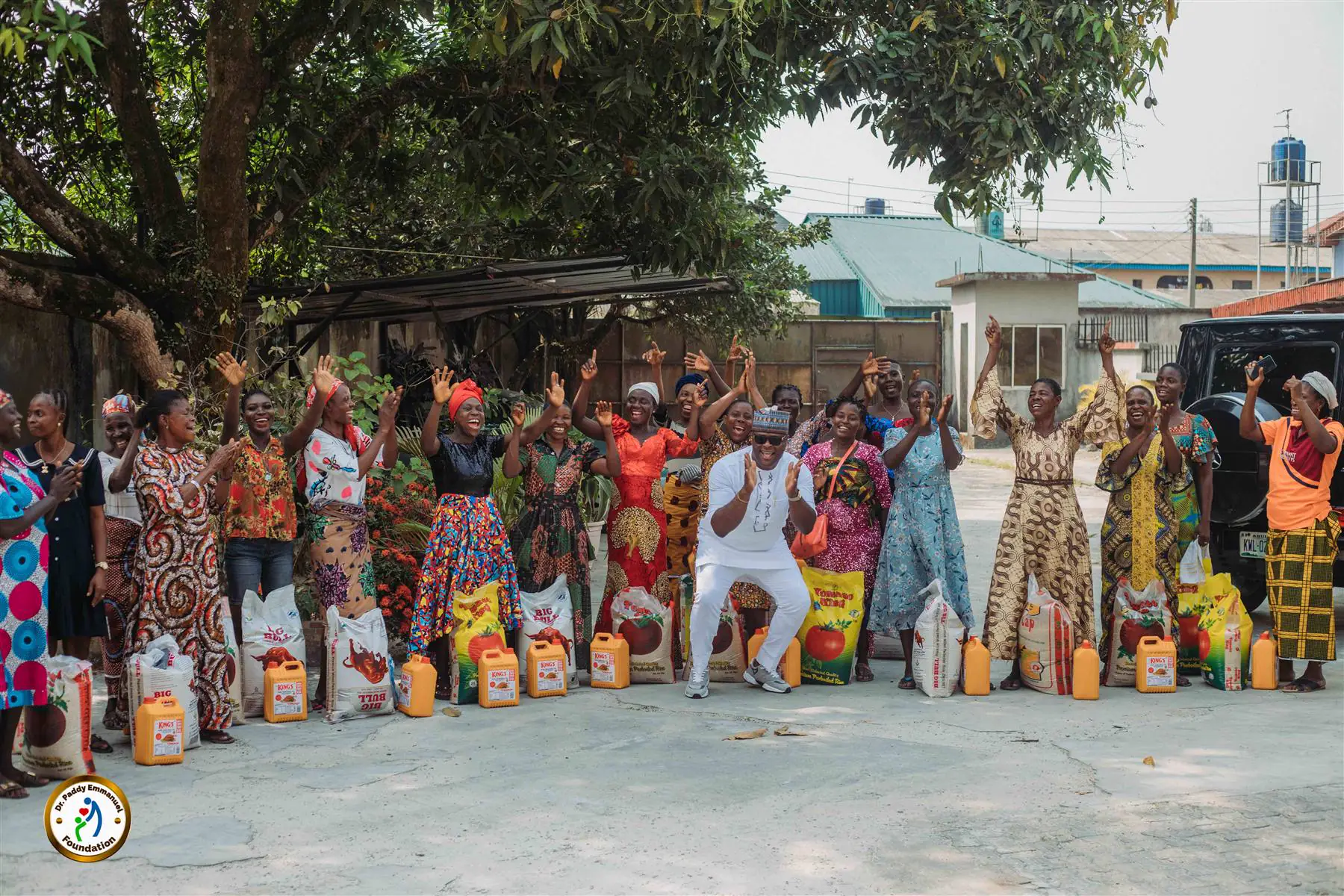 Dr Paddy Iyamu celebrating with women beside bags of rice at a Gift of Love event